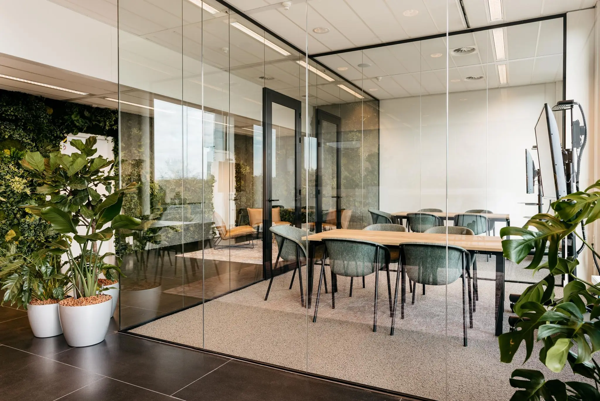 Vergaderruimte aan de Fascinatio Boulevard met glazen wanden, moderne meubels en diverse groene planten.